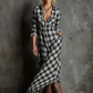Woman wearing a long plaid dress and cowboy boots against a textured wall.